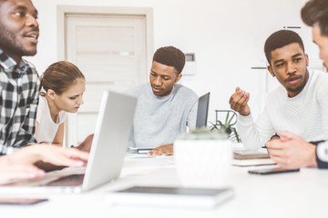 A team of young office workers, businessmen with laptop working at the table, communicating together in an office. Corporate businessteam and manager in a meeting. coworking.