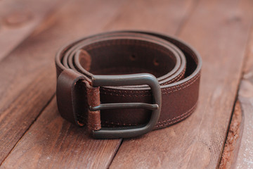Dark brown men's belt with buckley on a wooden desk