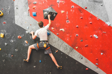 Sportsman climber moving up on steep rock, climbing on artificial wall indoors. Extreme sports and...