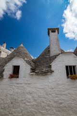 Fototapeta na wymiar Roofs of truli, typical whitewashed cylindrical houses in Alberobello, Puglia, Italy with amazing blue sky with clouds, street view, small windows and chimney