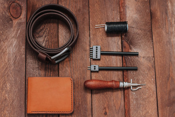 Leather products and leather tools on wooden desk. Mens belt and wallet