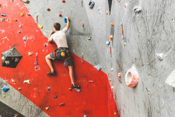 Sportsman climber moving up on steep rock, climbing on artificial wall indoors. Extreme sports and...
