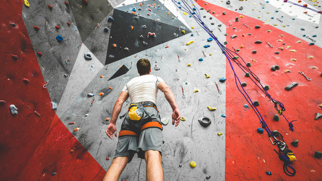 Sportsman climber is looking on steep rock, climbing on artificial wall indoors. Extreme sports and bouldering concept