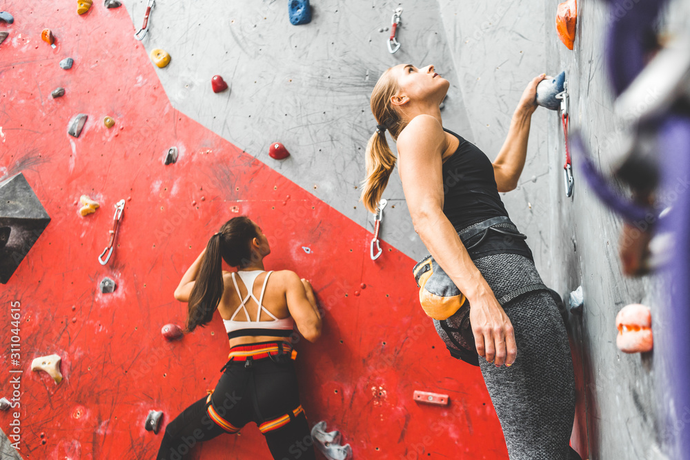 Wall mural athletes climber moving up on steep rock, climbing on artificial wall indoors. extreme sports and bo