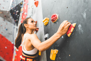 Sportswoman climber moving up on steep rock, climbing on artificial wall indoors. Extreme sports...