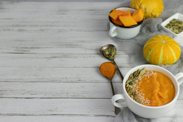 pumpkin cream soup in a ceramic plate on a white wooden background using gray textile, and small decorative pumpkin and spoons. copy space