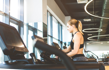 Fototapeta na wymiar The athletic woman dressed in a black sportswear running on the treadmill in the modern gym