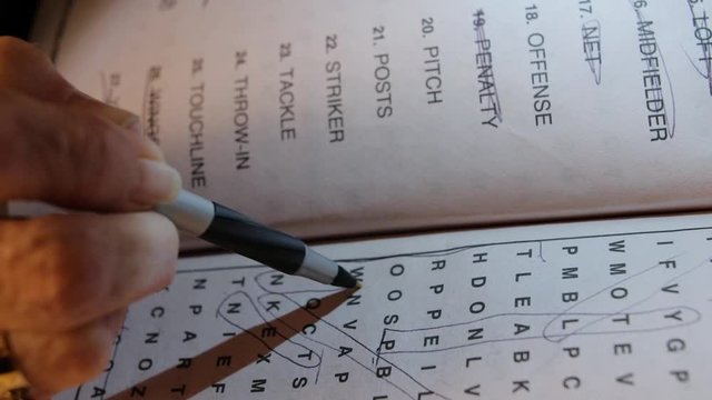 Closeup of female hand circling letters in word seek and find puzzle book.