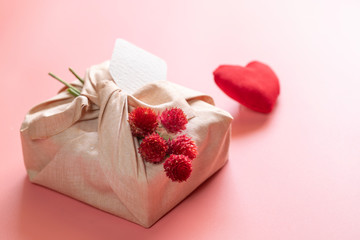 Stylish eco-friendly rustic gift wrapped in linen fabric with branch of red flowers on pink background. Copy space. Simple eco presents plastic free. Zero waste Valentine