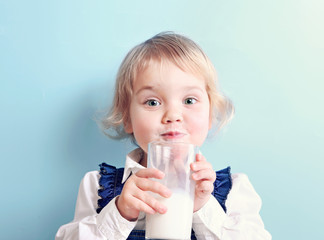 Child girl with glass of milk on blue background.Caucasian kid portrait.