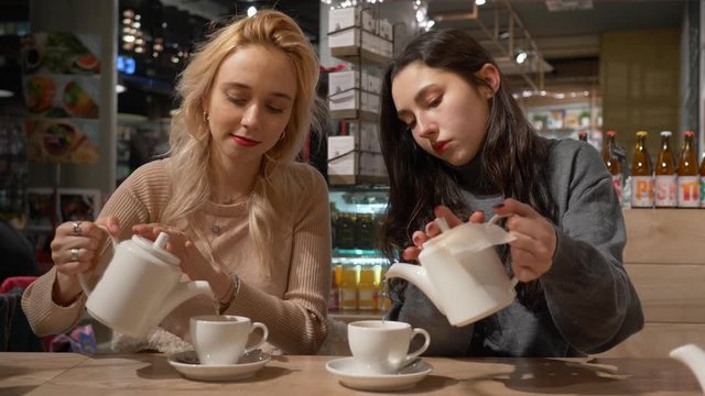 Two beautiful young women girlfriends drink tea sitting in cozy cafe hanging out together