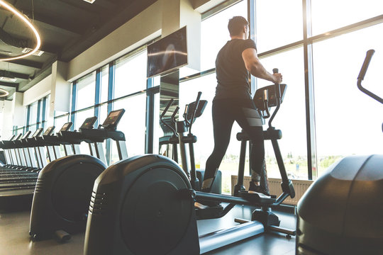 The athletic man dressed in a black sportswear running on the eleptic trainer in the modern gym