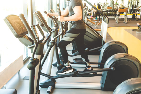 The athletic man dressed in a black sportswear running on the eleptic trainer in the modern gym
