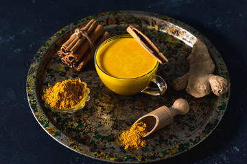 Golden turmeric milk on the dark background with spices cinnamon and ingredients