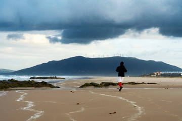  Young man running in a sandy beach by the Ocean. Awesome morning view with dramatic clouds over...