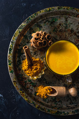 Golden turmeric milk on the dark background with spices cinnamon and ingredients