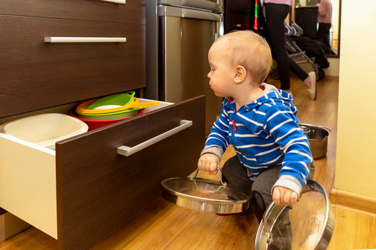 Cute curious baby exploring content of drawers in kitchen. Baby playing with kitchenware.