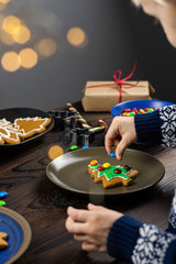 The child decorates with candys a gingerbread in the shape of a Christmas tree. Close up children's hands, lots of sweets on a wooden table.