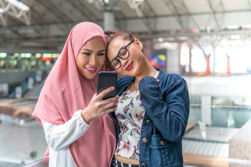 Two friends at the train station holding smartphone,