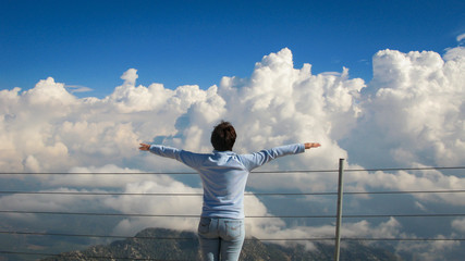 woman stands on top of a mountain near abyss on a background of blue sky and white clouds on a sunny day