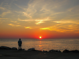 Fototapeta premium man on the seashore looks at dawn, blue sky and white clouds