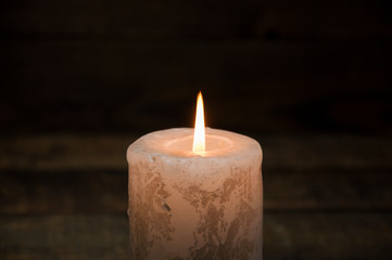 A large candle burns in the dark. On a wooden background.