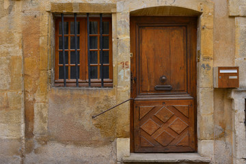 Porte bois à moulures et fenêtre à barreaux sur vielle façade en pierres tons jaunes, en...