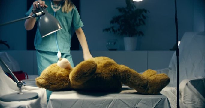 Cute little girl wearing doctor suit playing at home, pretending to be a surgeon, bandaging her teddy bear. Shot on RED Cinema camera with Cooke Prime lenses