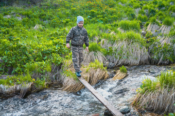 The boy crosses the river by a narrow plank