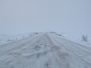 Fototapeta na wymiar Empty road covering by white snow and some dry grass at side way with cloudy climate in winter season.