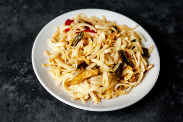 Asian food udon noodles with chicken and vegetables on a white plate on a stone background