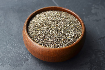 Uncooked raw chia seeds superfood in wooden bowl on dark stony background.