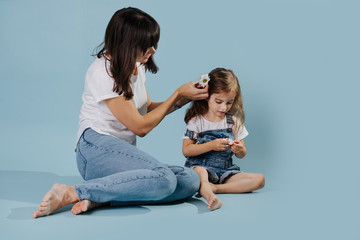 Obraz na płótnie Canvas Mum decorates daughter's hair with daisy sitting on floor