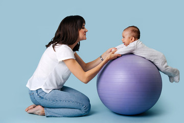 young mother plays fitness ball with her baby.