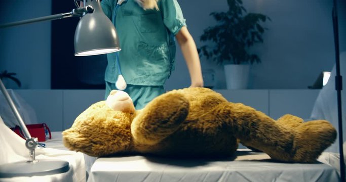 Cute little girl wearing doctor suit playing at home, pretending to be a surgeon, bandaging her teddy bear. Shot on RED Cinema camera with Cooke Prime lenses