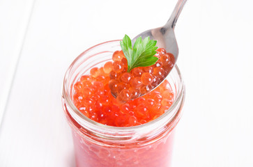 Red caviar in glass bowl on white wooden background