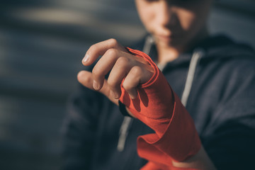 Close up view of young male hands with boxing bands. Boy prepares for a boxe workout by wrapping...