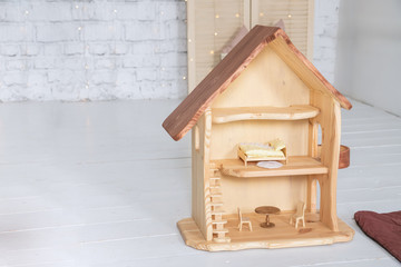 Puppet wooden house stands in the room. The doll house has three floors stuffed with mini furniture toys and doll. Baby expectation concept
