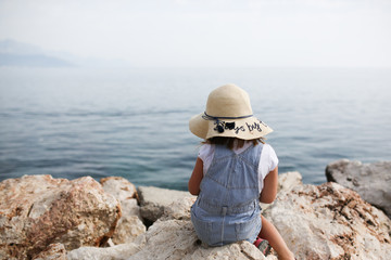 girl child sitting on stones in sea bay, looking