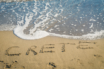 inscription Crete on the sand near the sea wave rest