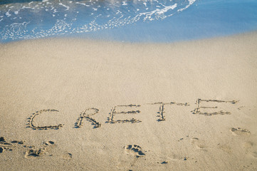 inscription Crete and footprints on the sand near the sea wave rest