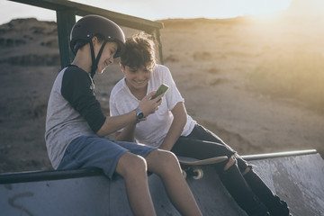 Couple of friends enjoying free time at the skatepark looking video of halfpipe tricks online. Teenagers having fun with skateboard sharing multimedia content with friend. Youth, communication concept