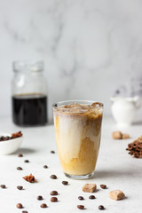 Cold brew coffee with spices and milk on light grey background. Spicy coffee with ice cubes.