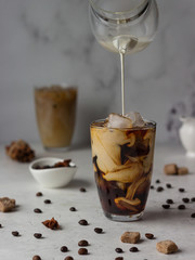 Ice coffee in a tall glass with cream being poured into it showing the texture of the drink. Spicy coffee with ice cubes.