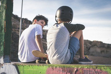 Back view of smiling teens talking about tricks and jumps with skateboard. Young boys sitting on...