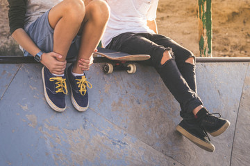 Close up of two young boys sitting on half pipe ramp, after nice tricks and jumps at the skatepark. Trendy teenagers enjoying free time at the skate park. Youth, togetherness and friendship concept. - Powered by Adobe