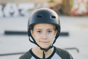 Fototapeta na wymiar Portrait of trendy young skater at the skatepark wearing helmet, looking in camera. Teenager enjoying sunny day outdoors in the city with skateboard. Youth, happiness, safety, sport, positive concept