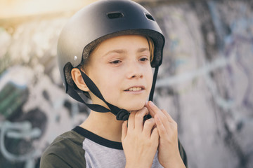 Fototapeta na wymiar Portrait of trendy young skater at the skatepark wearing helmet, looking away. Smiling teenager enjoying sunny day outdoors in the city with skateboard. Youth, health, safety, sport, positive concept