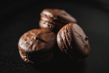 Chocolate french macaroon (sweet confection) with ganache on a black background. There is a place...