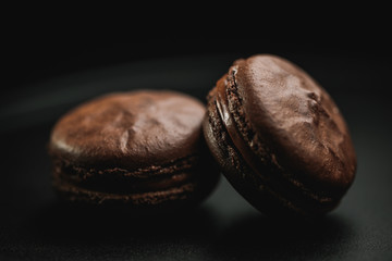 Chocolate french macaroon (sweet confection) with ganache on a black background. There is a place for text or logo